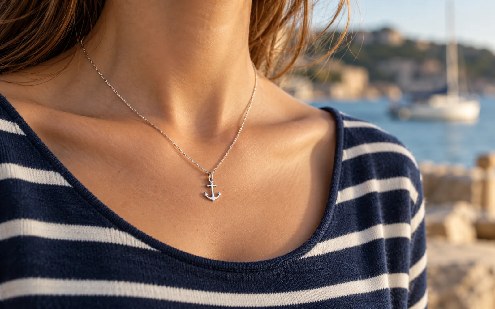 Collier fin à petit pendentif ancre porté sur un col de marinière, visage hors cadre