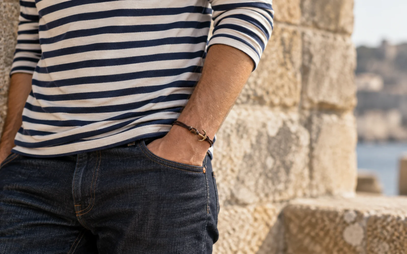 Personne en marinière et jean brut portant un fin bracelet en cuir au poignet, visage hors cadre